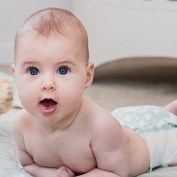 Baby with blue eyes lying on a bed wearing a nappy