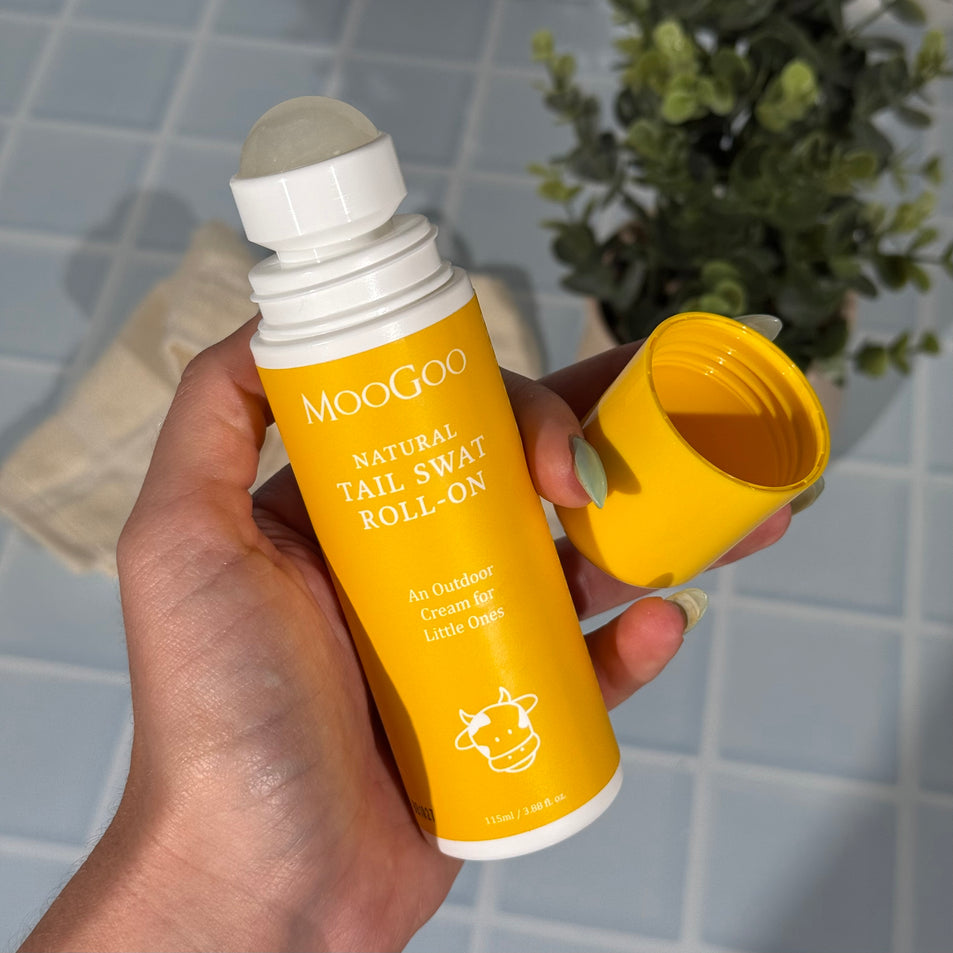 MooGoo Tail Swat Roll-On held in a hand with a plant in the background, gentle insect repellent cream for children and families, natural outdoor skincare