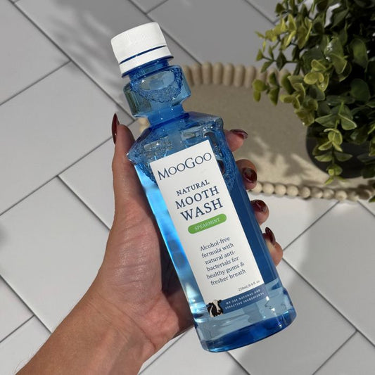 MooGoo Natural Moothwash Spearmint 250ml in hand on tiled bathroom counter with greenery, alcohol and fluoride free mouthwash