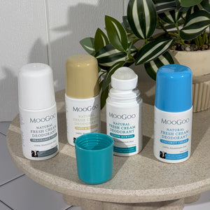 All four MooGoo Natural Fresh Cream Deodorants 60ml on a tray with a plant in the background. Includes Sensitive & Fragrance Free with a white lid, Oats & Honey with a caramel lid, Lemon Myrtle with a green/teal lid and Coconut Cream with a blue lid.