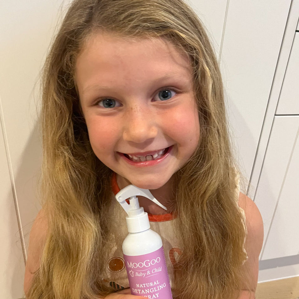 Smiling child holding MooGoo Baby & Child Natural Detangling Spray with, gentle conditioning spray for kids that banishes knots and tangles