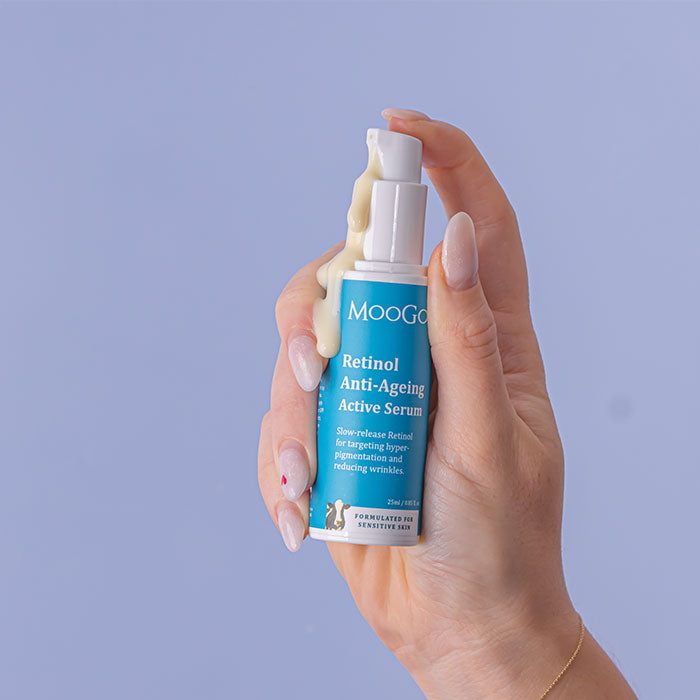 Hand holding a bottle of MooGoo Retinol Anti-Ageing Active Serum against a purple background